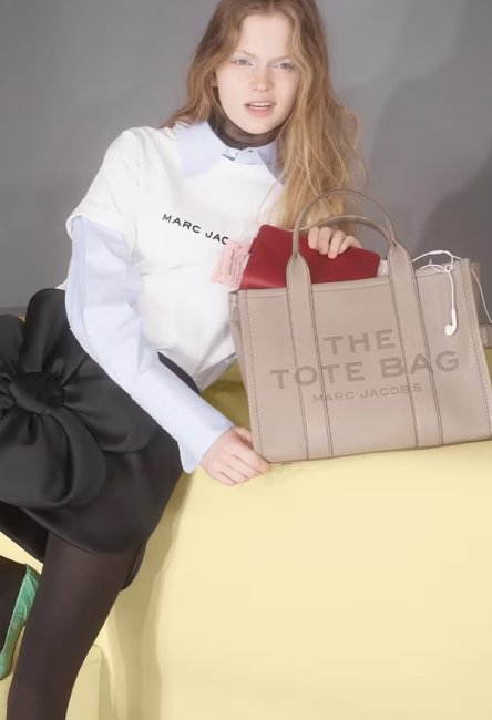 Modelo posando con sudadera blanca y bolso de mano beige The Tote Bag de Marc Jacobs